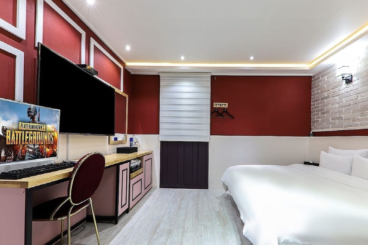 A bedroom with a bed, a desk with a computer, a chair, and a poster on the wall.