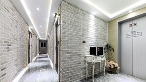A hallway with a brick wall, a white console table with a television, and a door labeled "HOTEL CHEESE". - Hotel Cheese Ulsan Samsan (Ulsan)