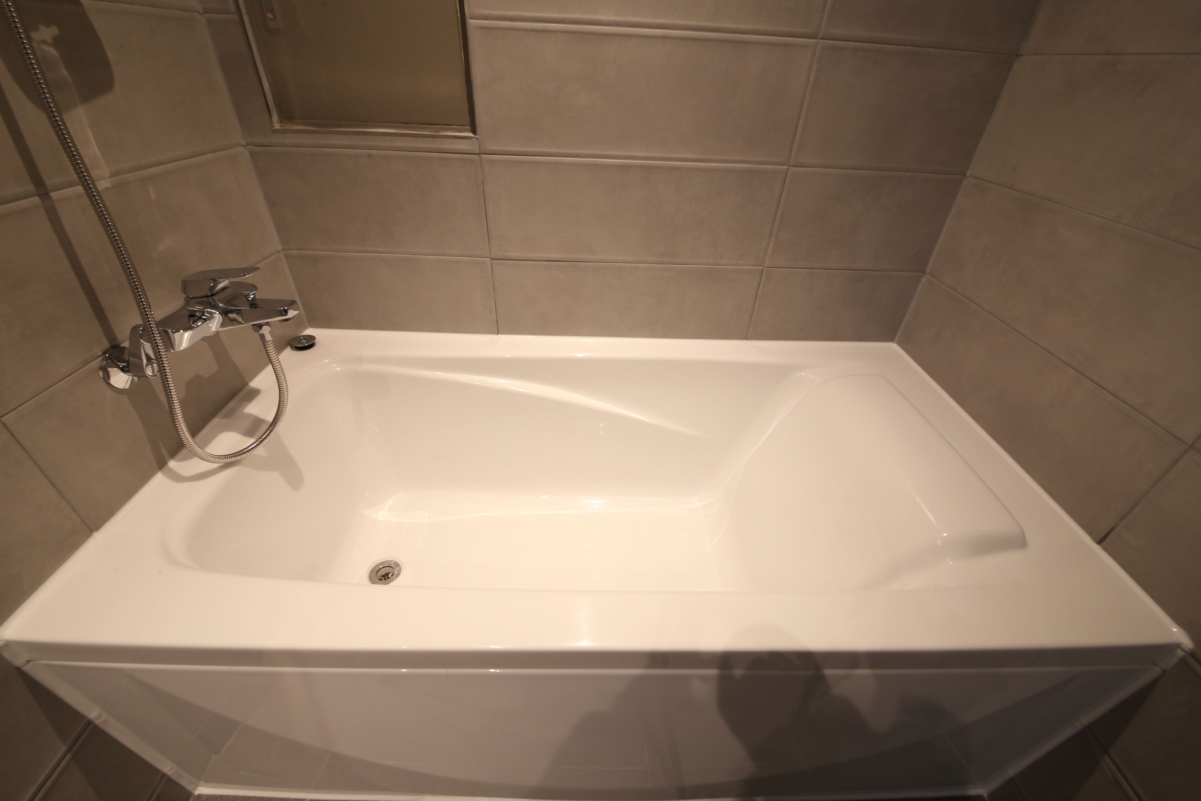 A rectangular bathtub with a handheld showerhead, set against beige tiled walls.