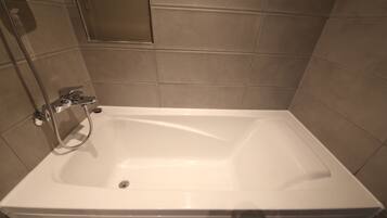 A rectangular bathtub with a handheld showerhead, set against beige tiled walls.