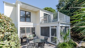 Een tweelaags huis met een balkon, een terras met een tafel en stoelen, en een overdekt buitengebied.