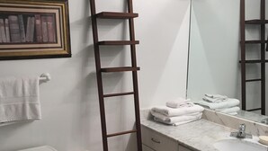 A bathroom with a toilet, a wooden ladder, a marble sink, and a framed picture on the wall.