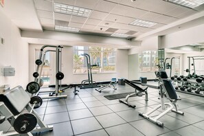 Un gimnasio con equipo de ejercicio variado, ventanas amplias y un espejo.