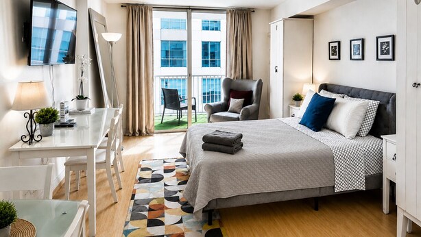 A modern hotel room with a bed, desk, chair, and a view of the outside.