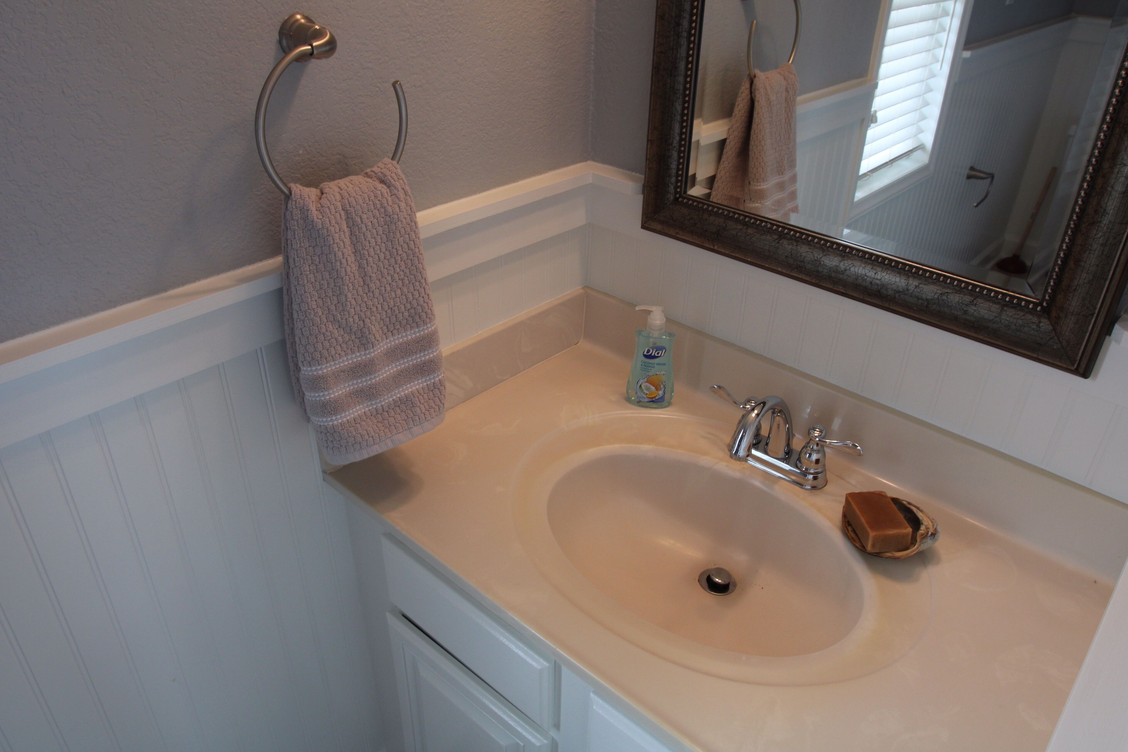 A bathroom with a beige sink, a mirror, a towel rack, and a soap dispenser.