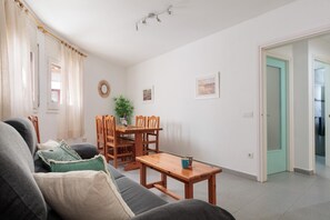 Un soggiorno con un divano, un tavolo da pranzo, sedie, un tavolino e una porta che dà su un'altra stanza.