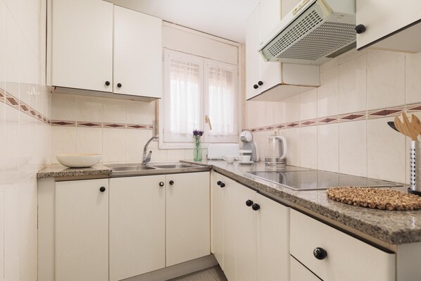 A kitchen with white cabinets, a granite countertop, a sink, and a window with curtains. - DUPLEX APARTMENT TOSSA Near Beach (Tossa de Mar)