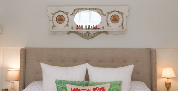 A bedroom with a large bed, two bedside lamps, a decorative mirror, and a shelf with figurines.