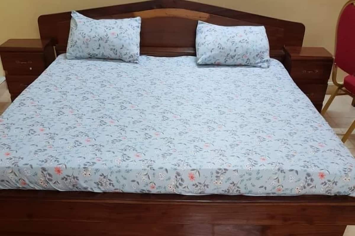 Un lit avec une couvre-lit à motifs floraux et deux oreillers, une tête de lit en bois et un sol carrelé.