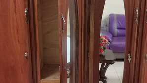 Un armario de madera con puerta espejada, un sofá morado y una pequeña mesa con flores al fondo.