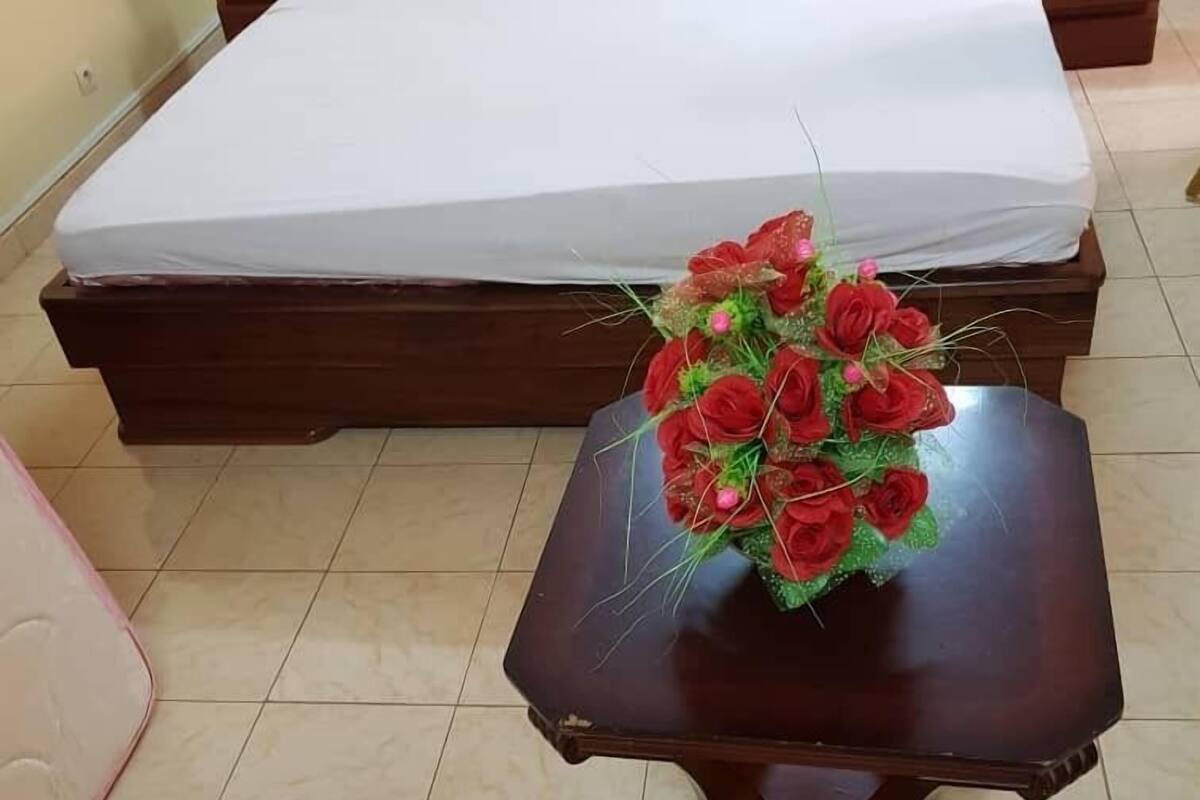 Une chambre à coucher avec un lit, une table de chevet ornée d’un bouquet de roses rouges et une commode.