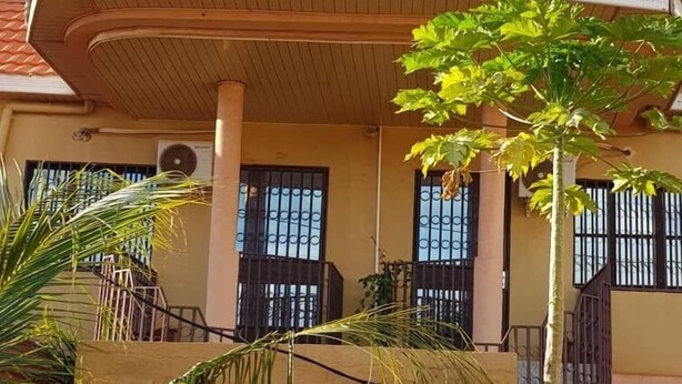 Un edificio de dos pisos con techo de tejas rojas, un pequeño ventanuco y un balcón con barandillas de metal.