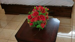 Un dormitorio con cama, almohadas y una mesa con un ramo de rosas rojas.