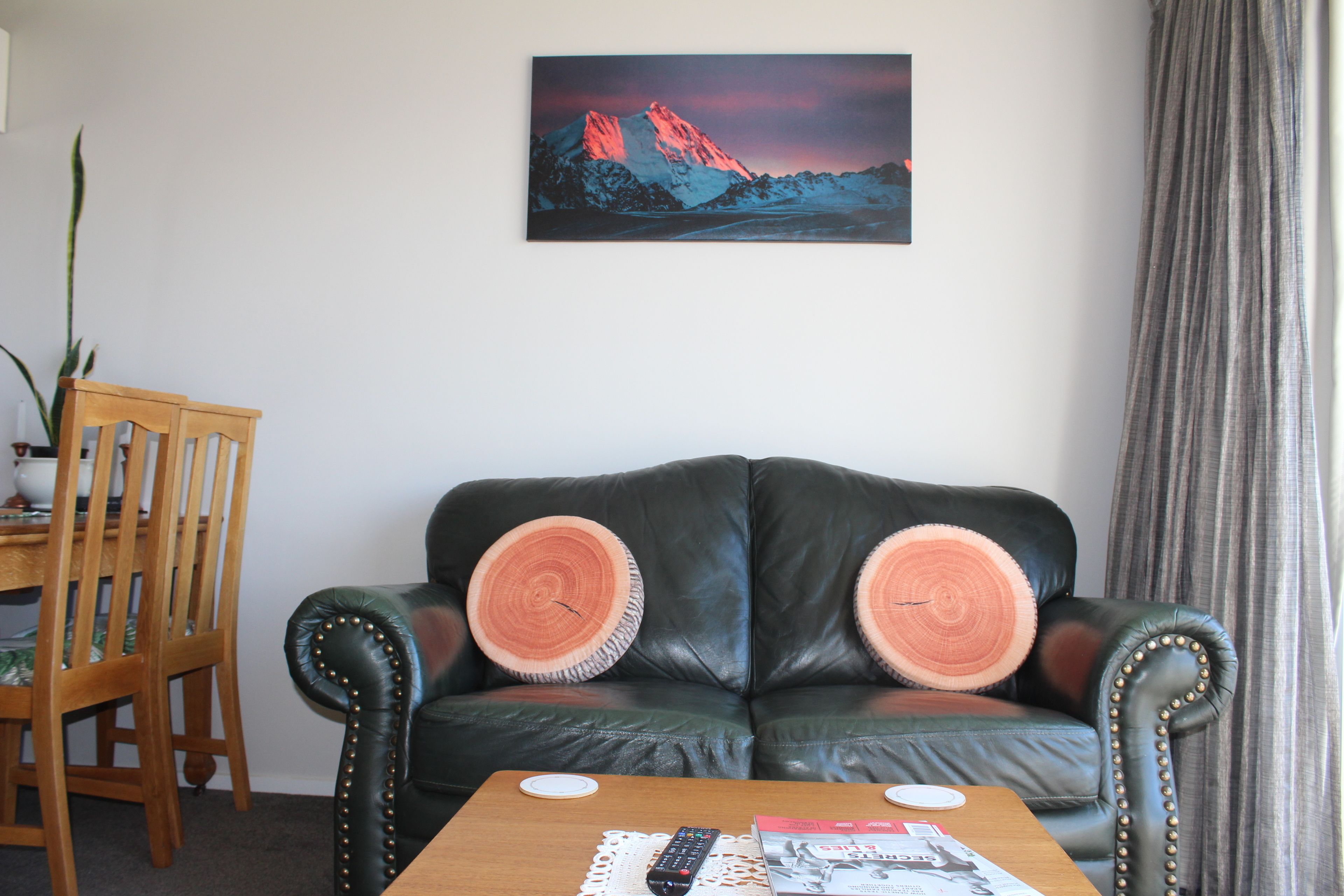A living room with a leather sofa, wooden dining table, and a painting of a mountain landscape.