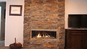 Una chimenea de piedra con un televisor arriba, un cuadro en la pared y una cesta en el suelo.
