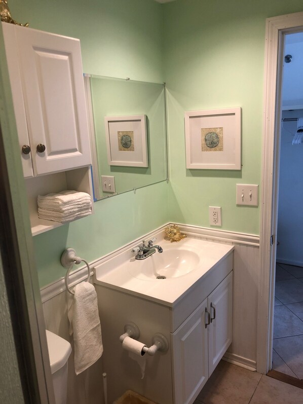 A bathroom with a white sink, a toilet, and a mirror. There are two framed pictures on the wall. - Oceanview Studio Condo (Hampton)