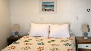 Een bed met een witte quilt met een patroon van slippers, twee witte kussens en een ingelijst strandlandschap aan de muur.