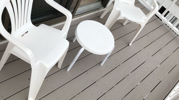 Twee witte plastic stoelen en een kleine ronde tafel op een houten terras.