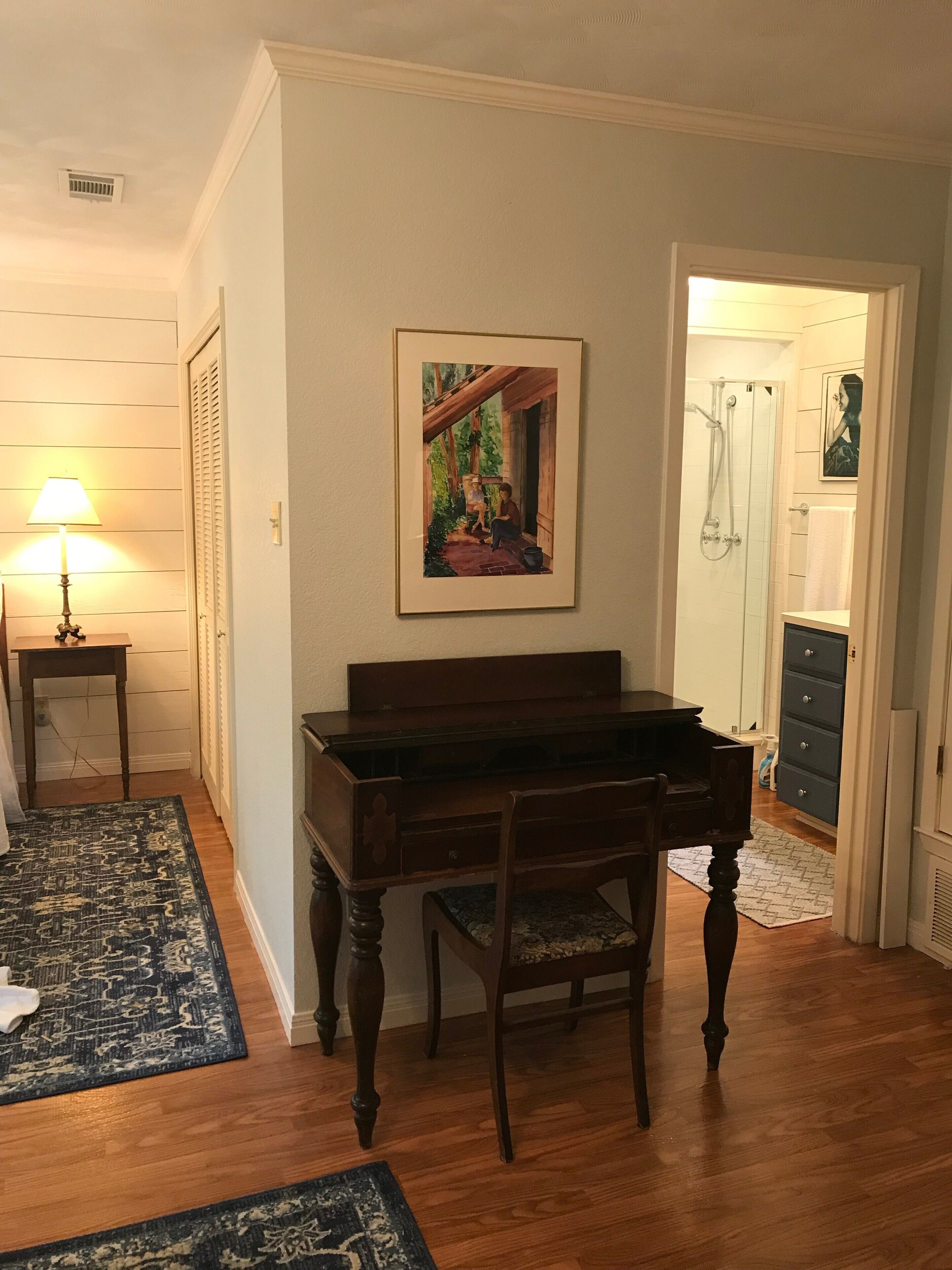 A room with a piano, a framed painting, a lamp, and a door leading to a bathroom.