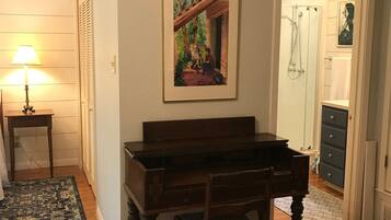 A room with a piano, a framed painting, a lamp, and a door leading to a bathroom.