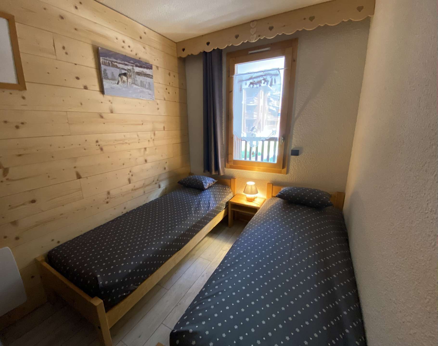 A small, cozy room with two single beds, a window with a view, and a wooden wall.