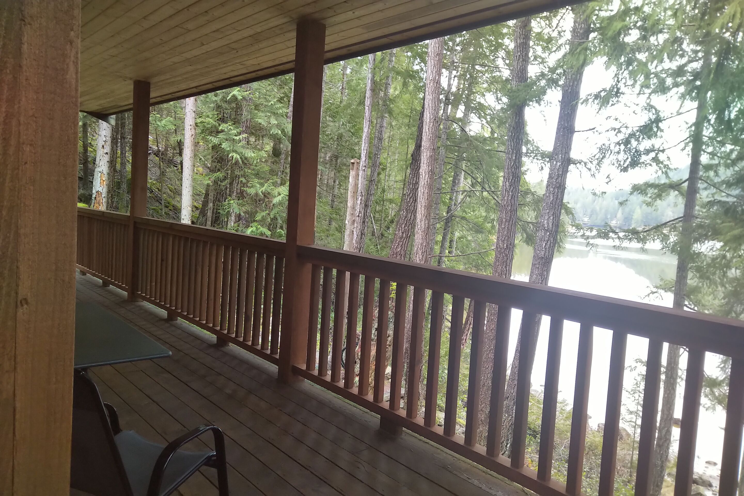 A wooden deck with a railing overlooking a forested area with a river.