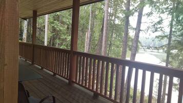 A wooden deck with a railing overlooking a forested area with a river.