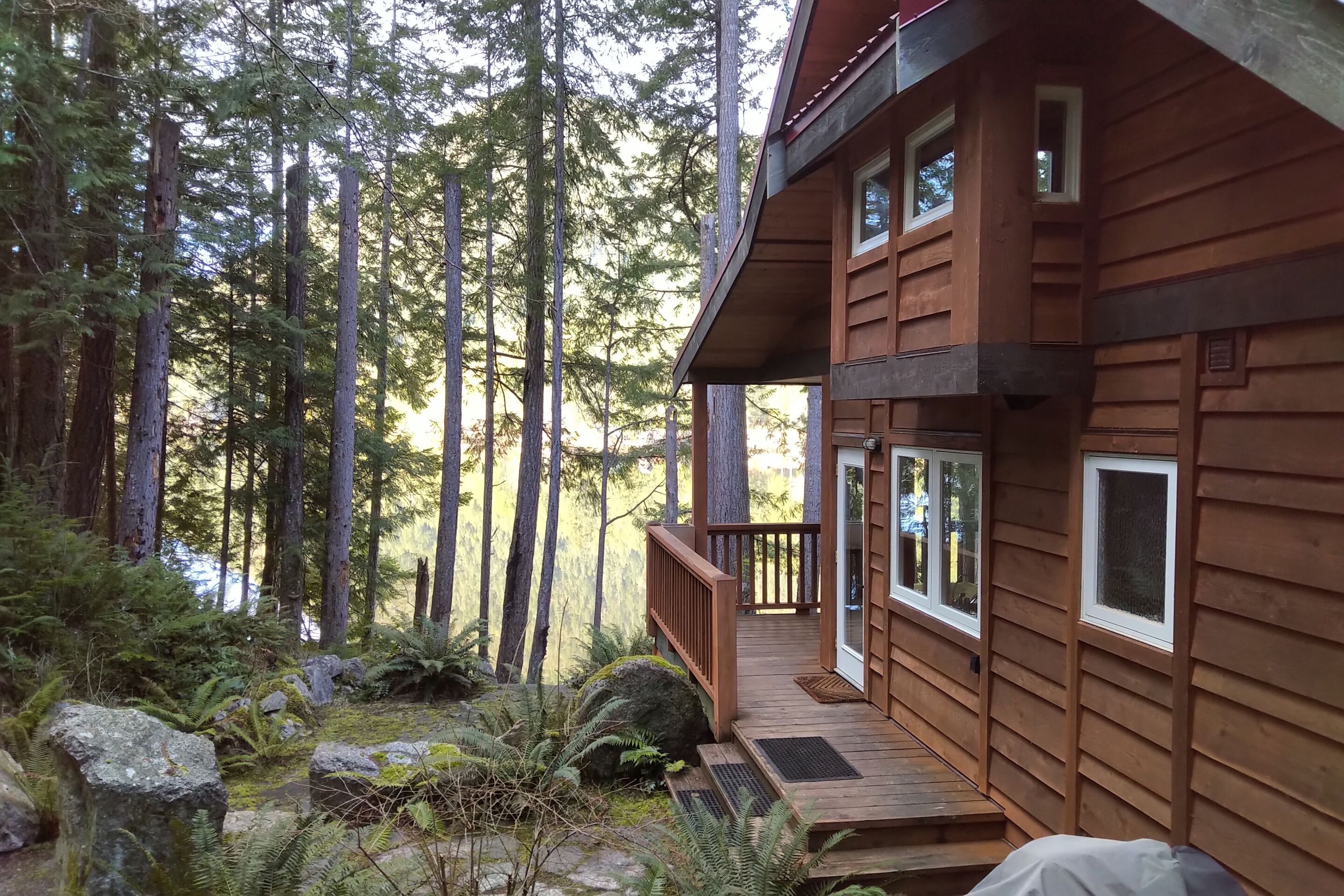Une cabane en bois dotée d’une terrasse, entourée de grands arbres et d’un paysage rocheux.