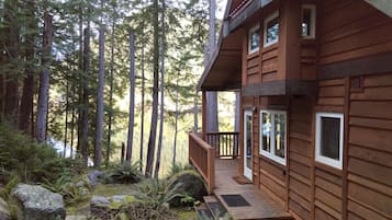 Une cabane en bois dotée d’une terrasse, entourée de grands arbres et d’un paysage rocheux.