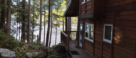 A cabin with a deck overlooking a forested area and a body of water.
