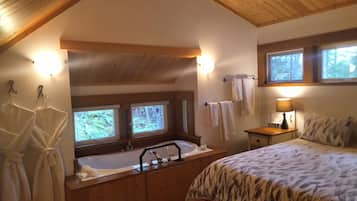 Une chambre dotée d’une grande baignoire, de deux fenêtres, d’un lit recouvert d’une couvre-lit à motifs et d’une table de chevet avec une lampe.