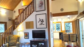Un salon avec un escalier en bois, un téléviseur et des œuvres d’art encadrées accrochées aux murs.