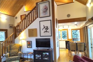 A living room with a wooden staircase, a television, and framed artwork on the walls.