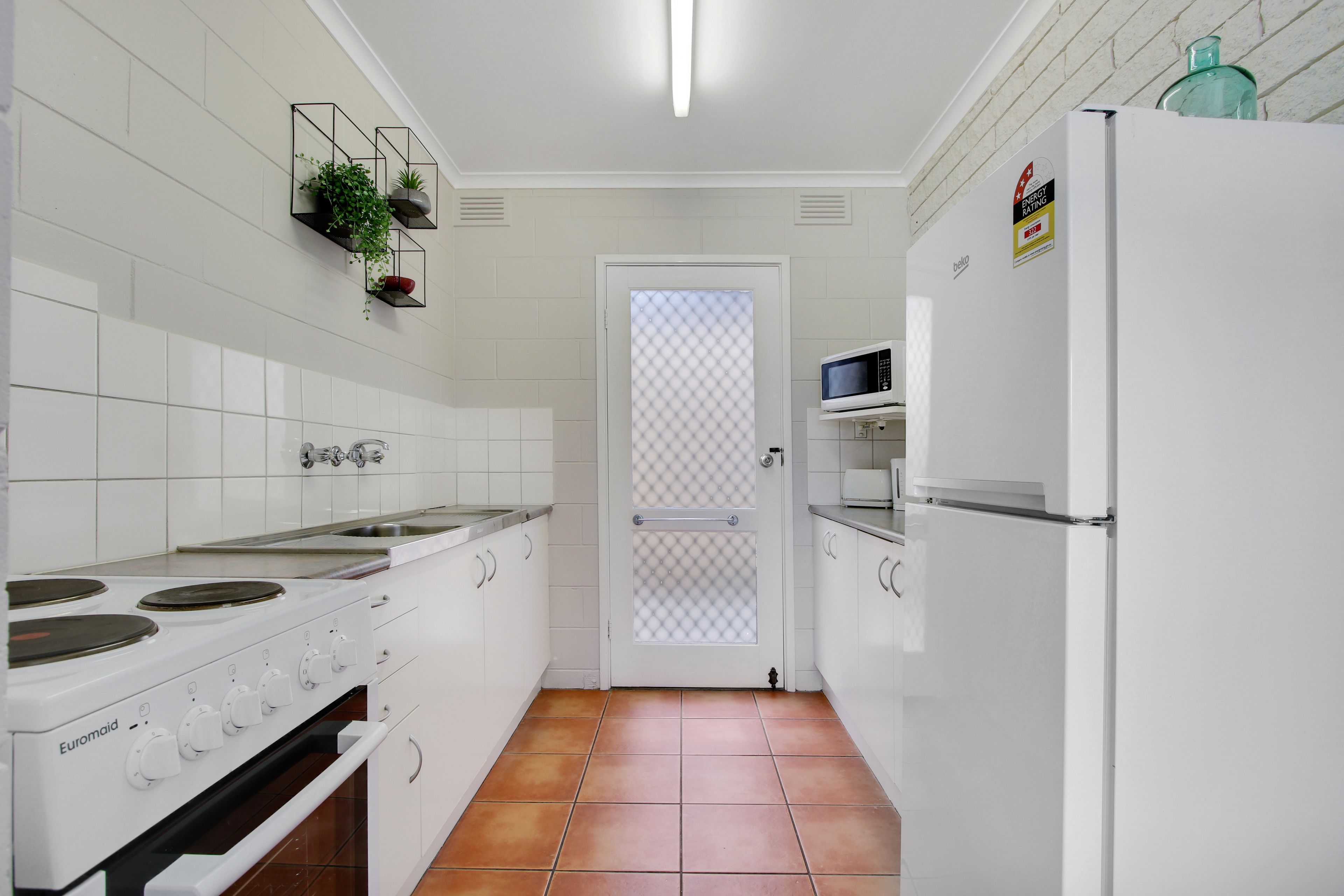A kitchen with white cabinets, a stove, a microwave, and a refrigerator.