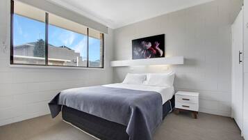 A bedroom with a bed, a nightstand, a window, and a wall-mounted artwork.