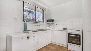 A kitchen with white cabinets, a microwave, a stove, and a window with a view of palm trees.