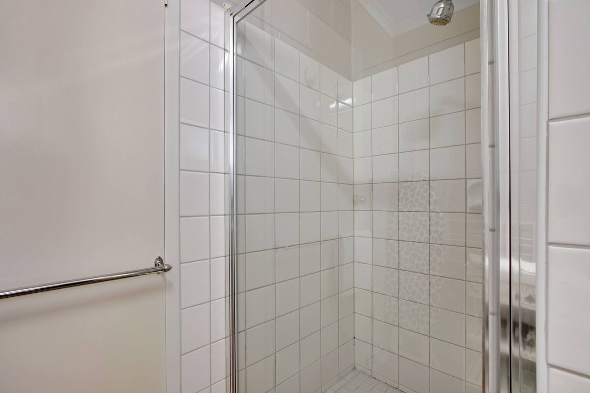A glass-enclosed shower with white tiles and a metal handrail.