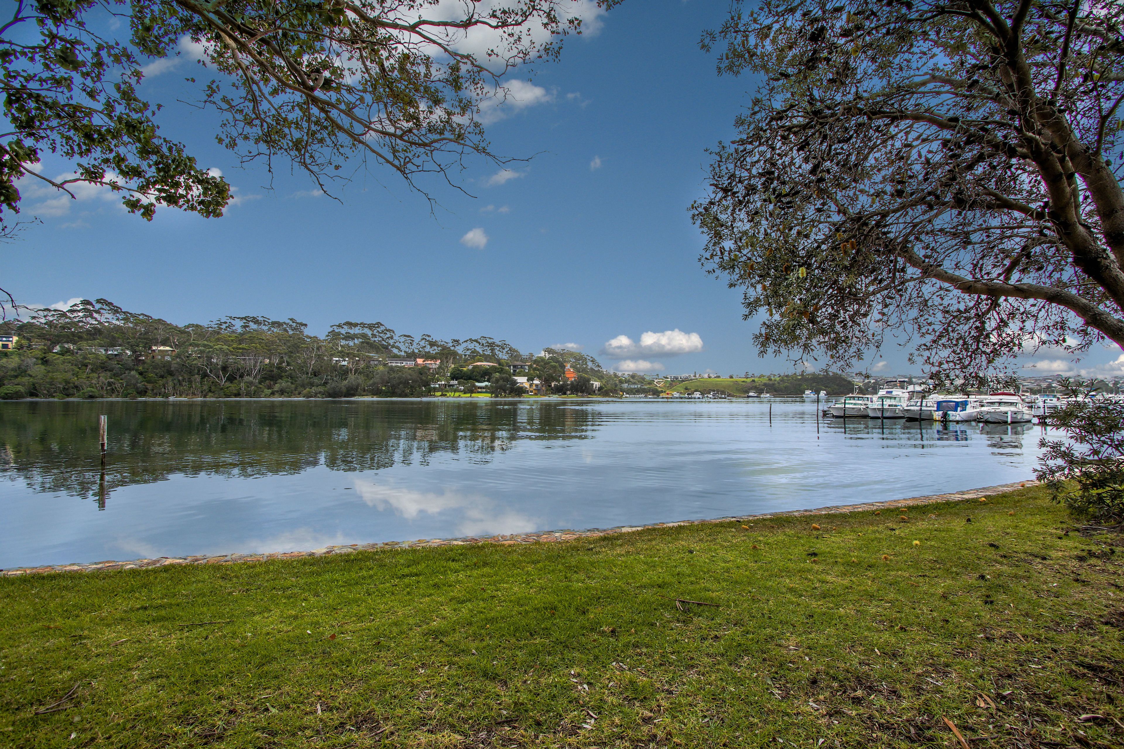 A calm lake with boats docked on the right, surrounded by grassy banks and trees.