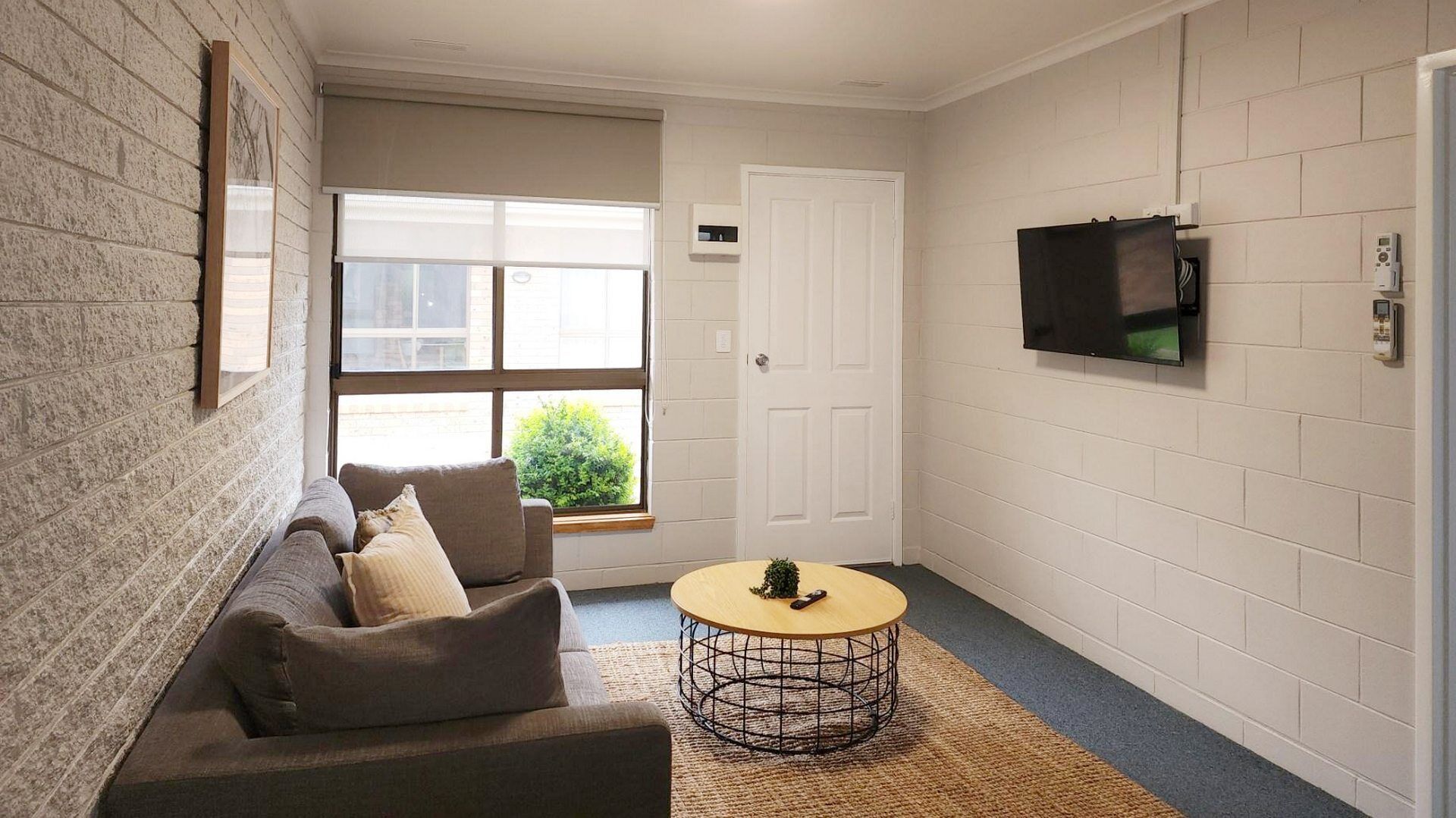 Um espaço compacto para relaxar, com um sofá, uma mesa de centro redonda e uma TV fixada na parede.