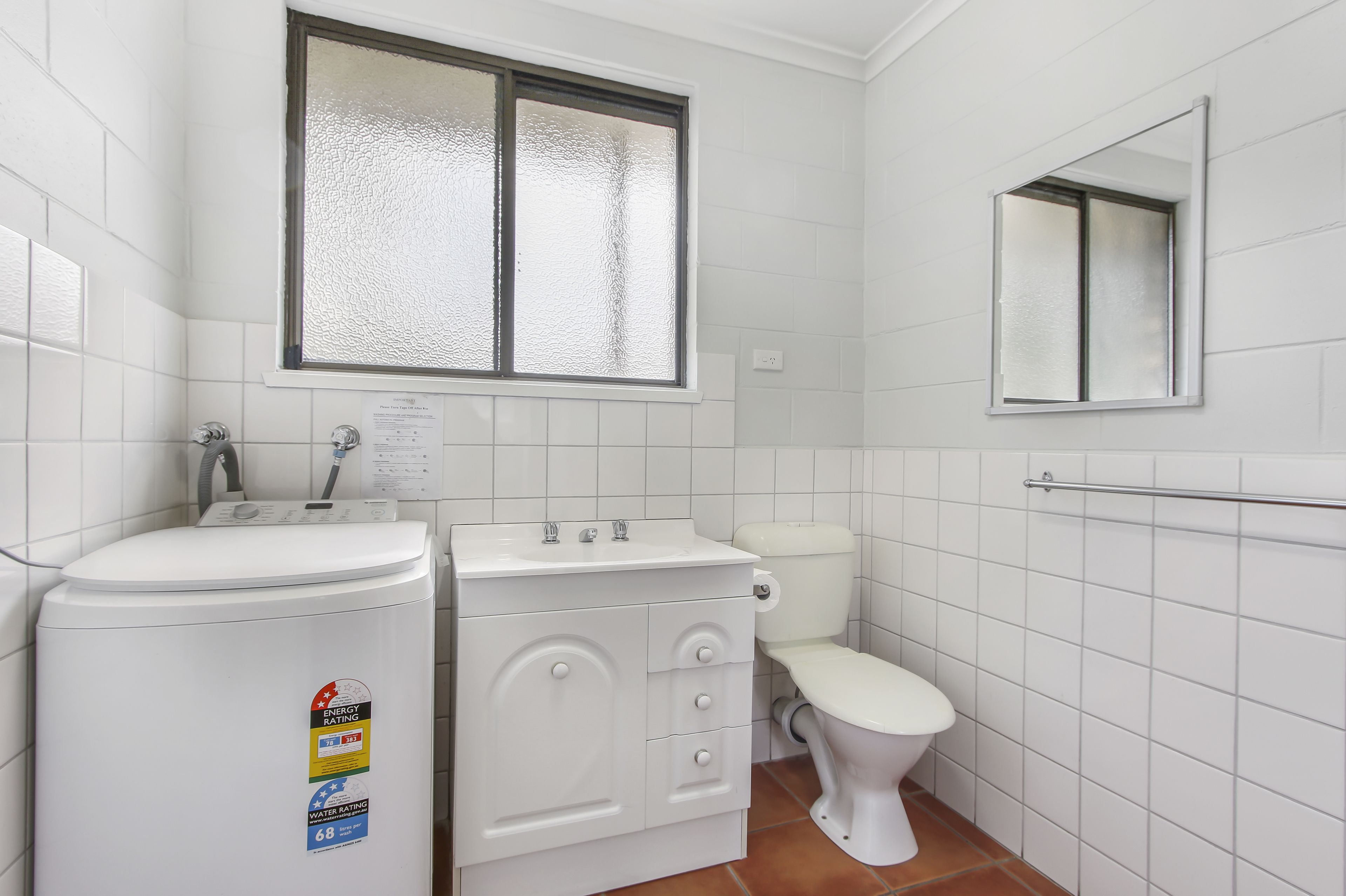 A small, white bathroom with a toilet, sink, and mirror.
