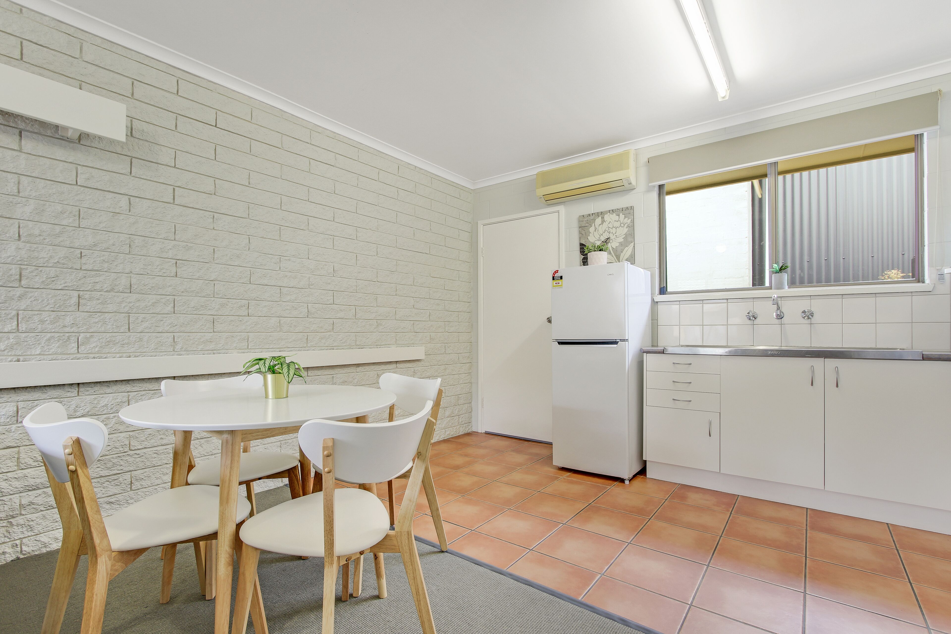 A compact kitchen with white cabinets, a white refrigerator, and a window with blinds.