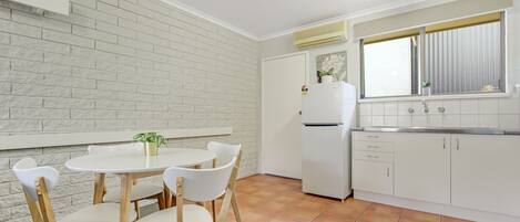 A compact kitchen with white cabinets, a white refrigerator, and a window with blinds.