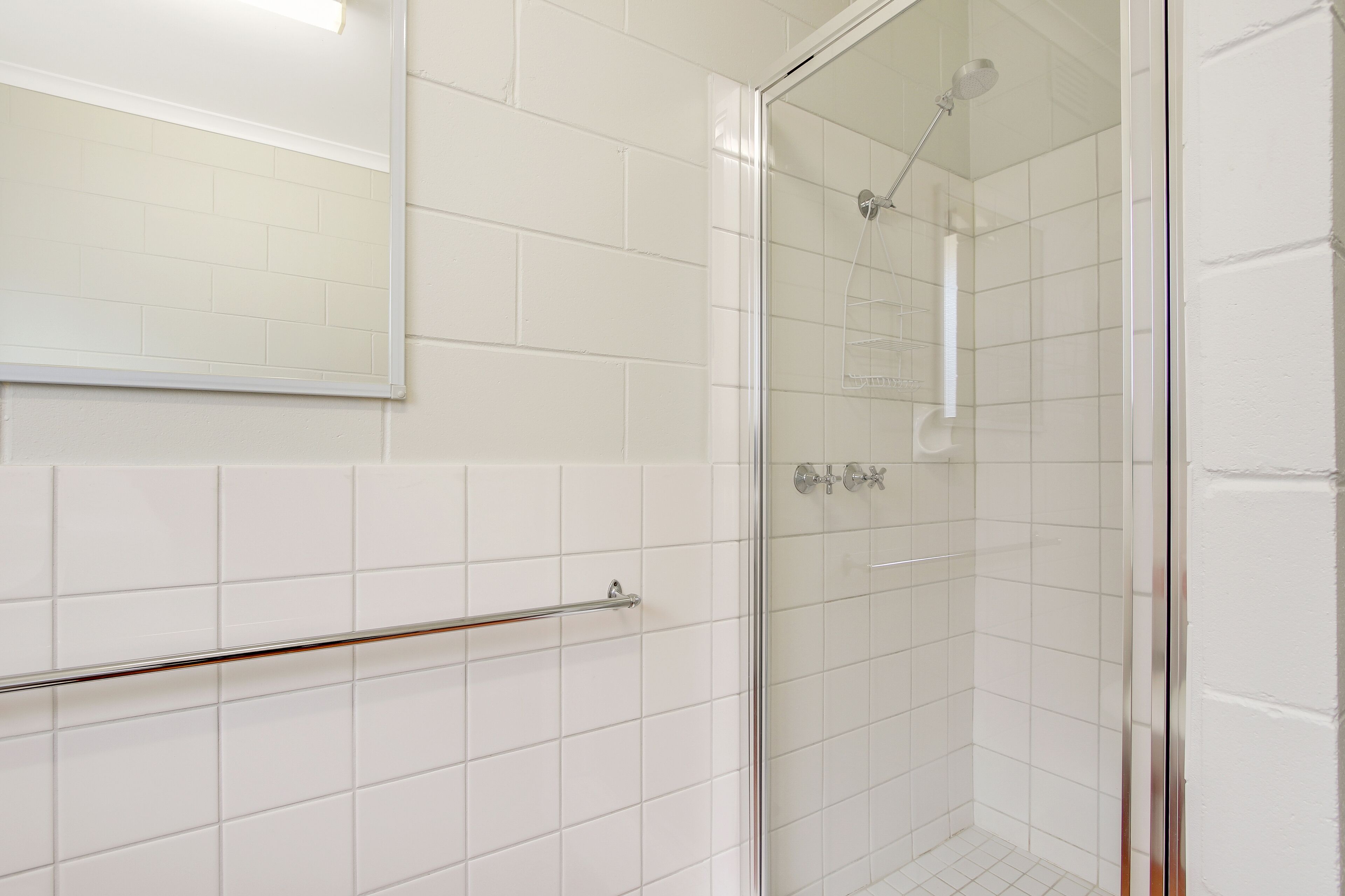 A bathroom with white tiled walls, a glass shower enclosure, and a metal towel rack.