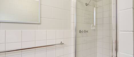 A bathroom with white tiled walls, a glass shower enclosure, and a metal towel rack.