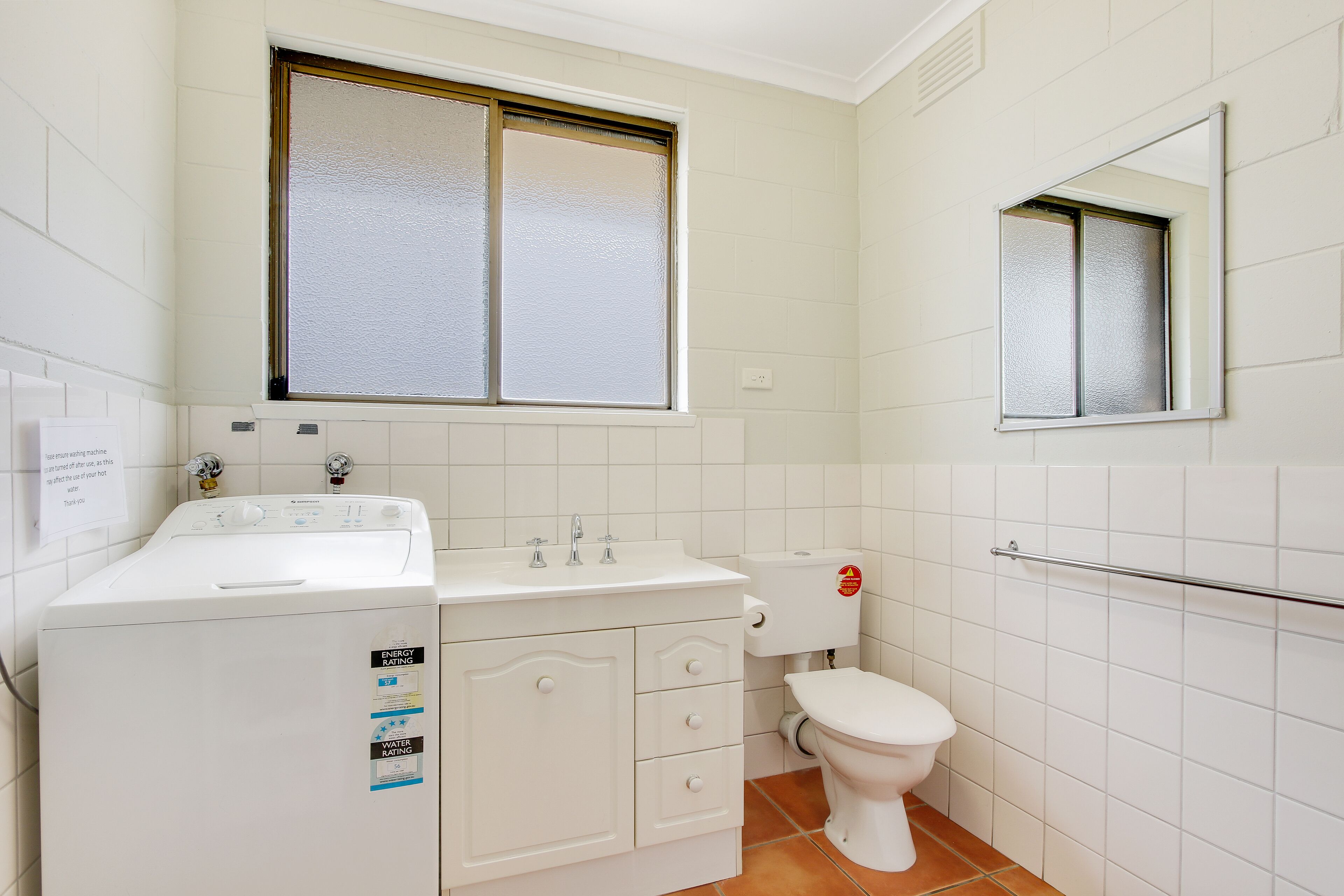 Un baño pequeño con lavadora, inodoro y ventana con vidrio esmerilado.