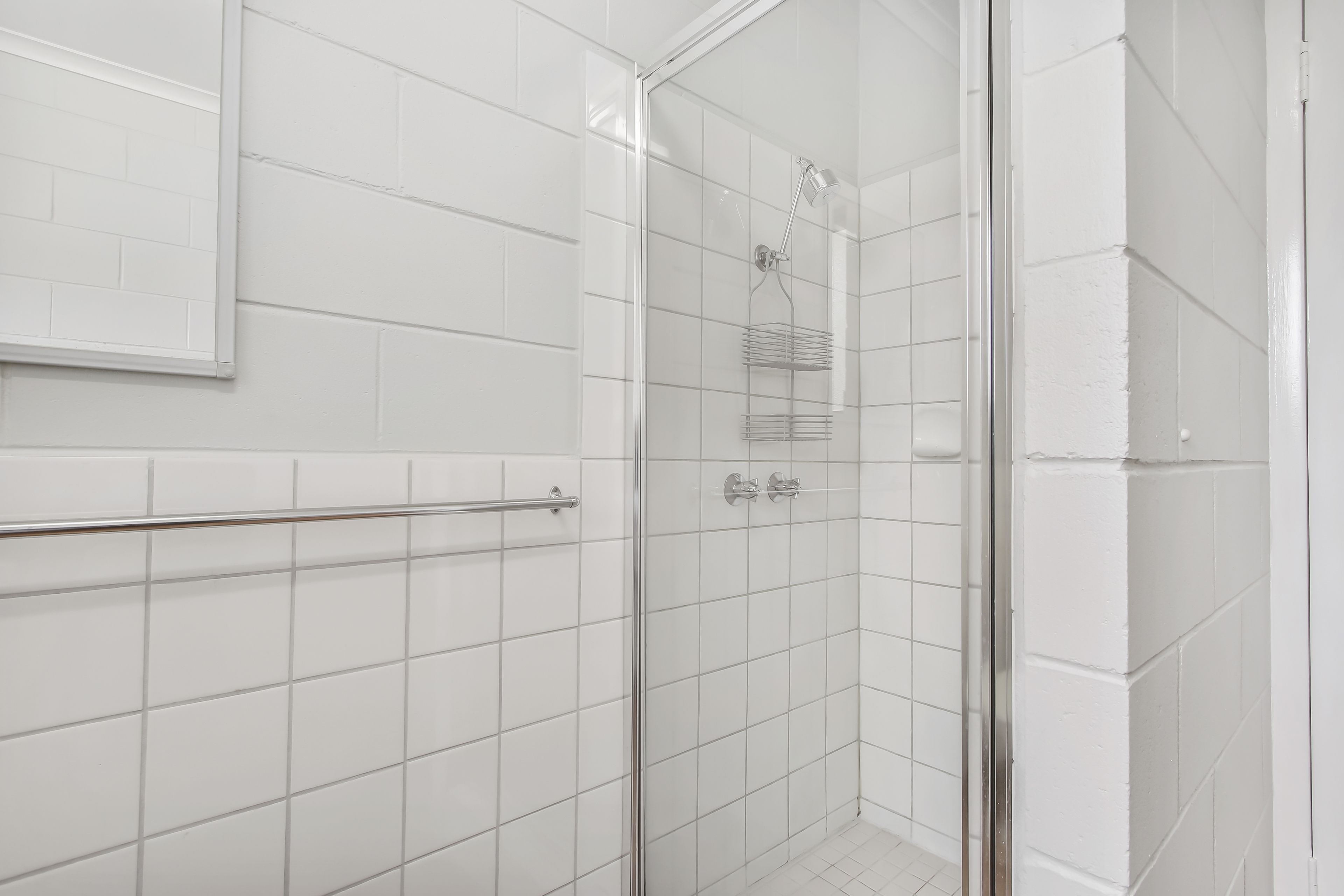 Un baño moderno con azulejos blancos, cabina de ducha de cristal, toallero y ducha.