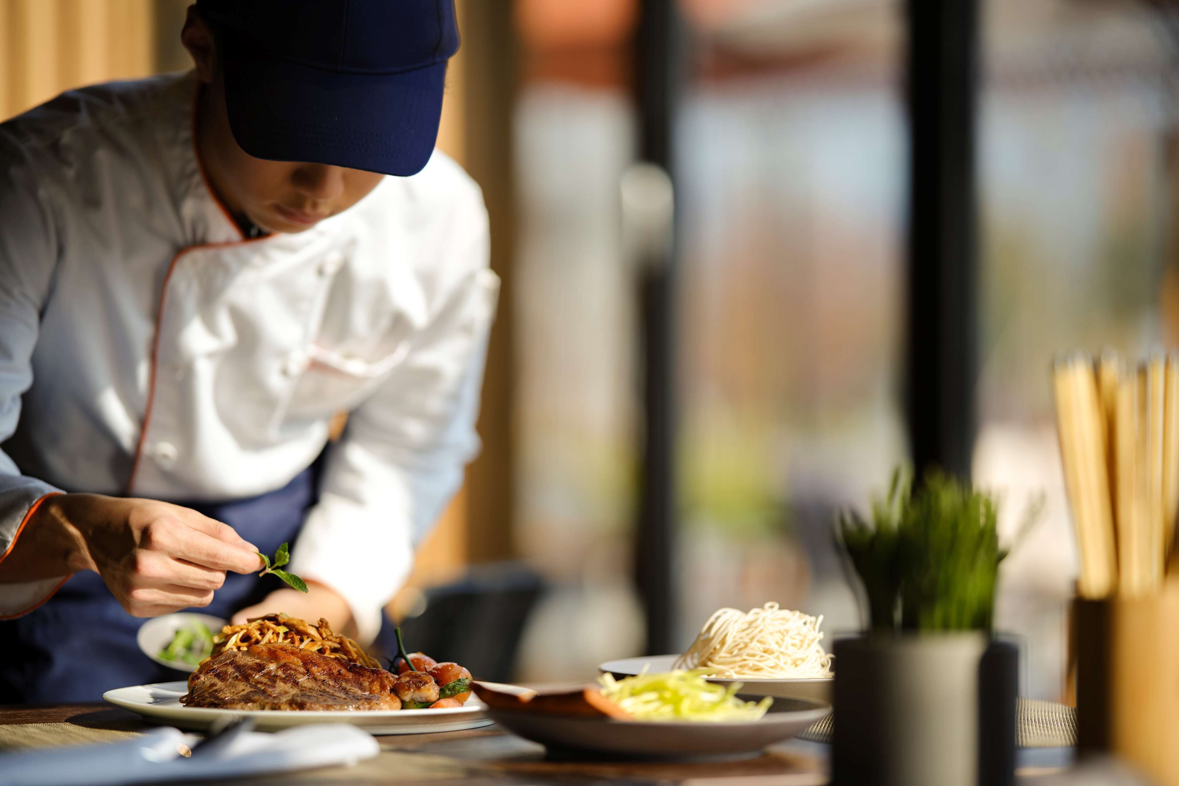Un chef préparant des plats dans une cuisine, avec une fenêtre en arrière-plan.