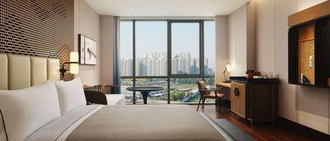 A modern hotel room with a large bed, a dining table, and a view of the cityscape.