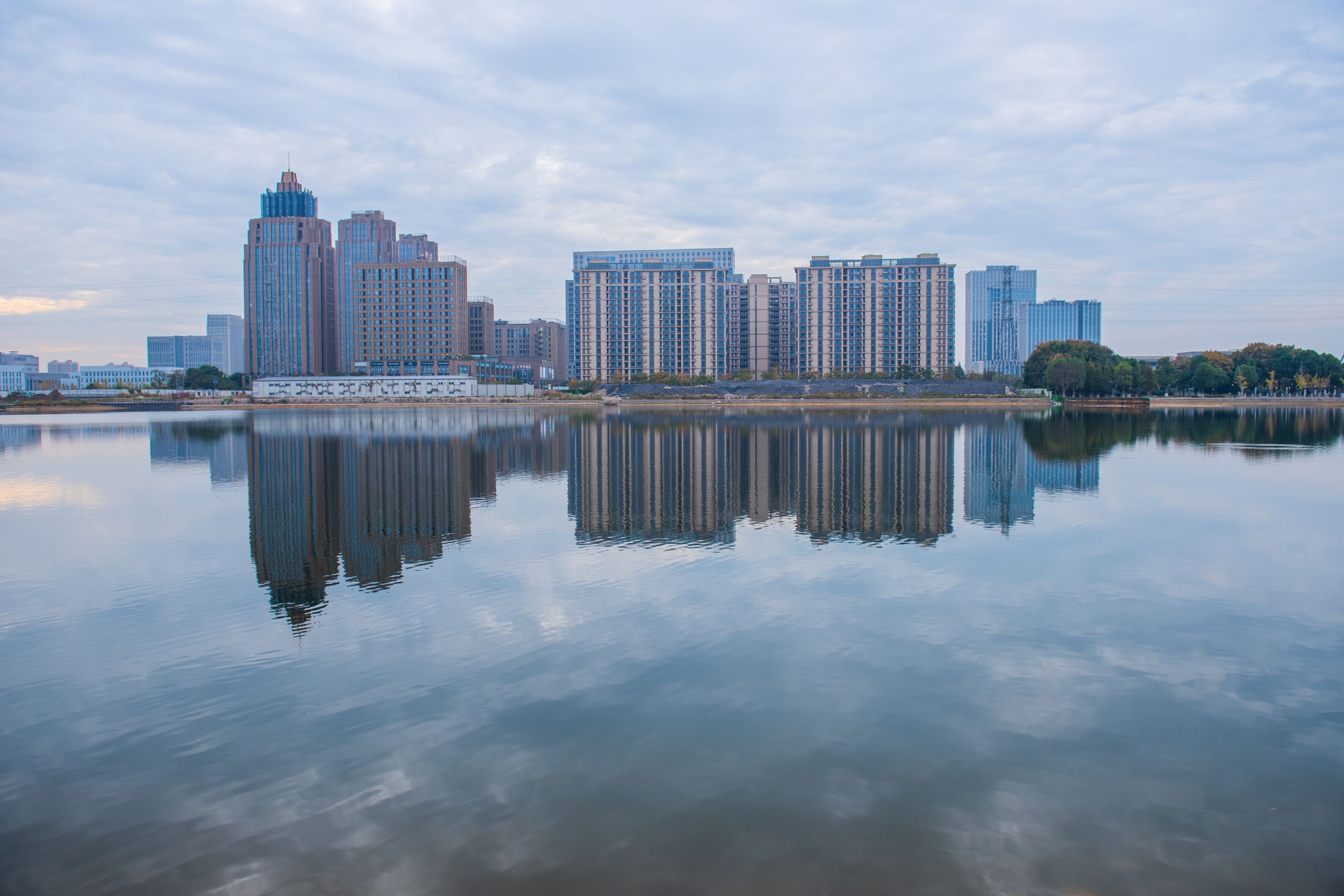 A city skyline reflected in calm water, featuring high-rise buildings and a clear sky.