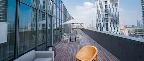 A rooftop terrace with a white sofa, wicker chairs, and a table with umbrellas.